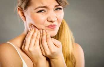 Person holding their jaw with a pained expression, suggesting toothache or discomfort.