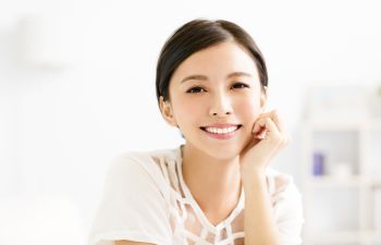 Person smiling and resting chin on hand, wearing a white top in a bright room.