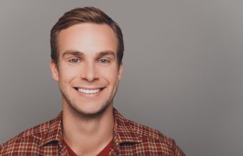 A person with short hair smiling, wearing a plaid shirt, against a plain background.