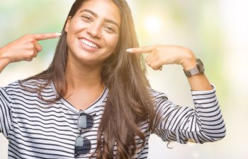 A person wearing a striped shirt points at their smiling face, with sunglasses hanging from the shirt.
