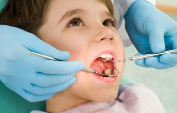 A child receives a dental check-up. A dentist uses a mirror and dental tool while wearing blue gloves.