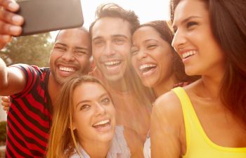 A group of five people smiling and taking a selfie in bright sunlight.