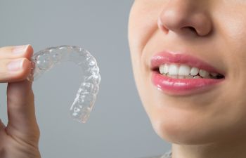 Person holding a clear dental aligner near their mouth, showing teeth.