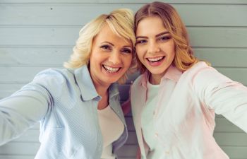 Two people smiling and taking a selfie in front of a light blue wooden wall.