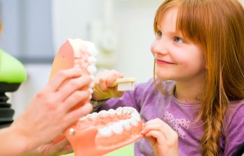 A child learns to brush teeth using a dental model in a classroom setting.