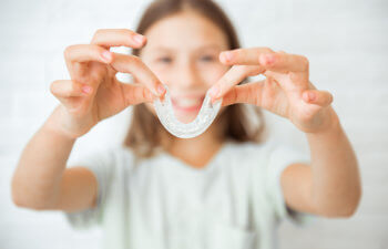A person holding a clear dental retainer with both hands, smiling in the background.