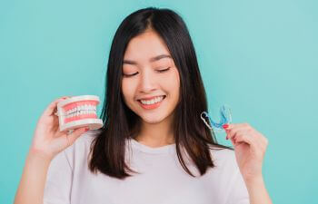 Young Asian woman holding a dental model and an orthodontic retainer.