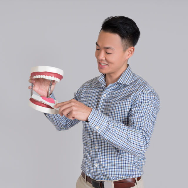 A person in a checkered shirt holding a large dental model of teeth and gums against a plain background.