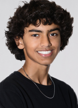 A person with curly hair smiles at the camera, wearing a black shirt and a thin chain necklace.