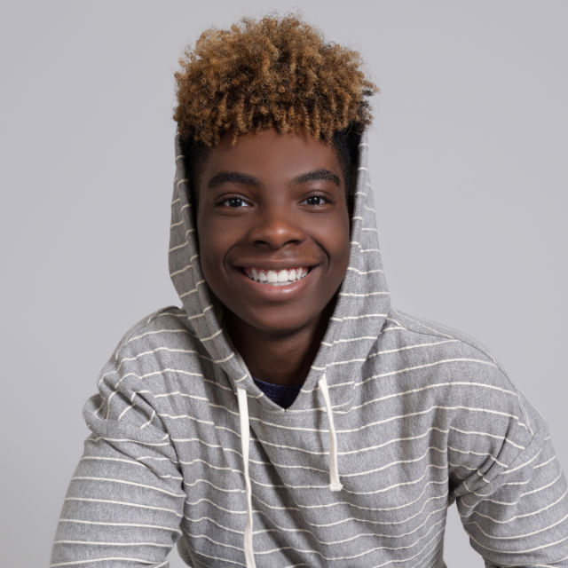 A person wearing a gray striped hoodie smiles at the camera against a plain background.