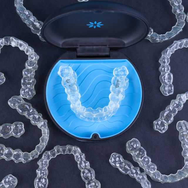 Clear dental aligners arranged around an open blue case on a dark background.