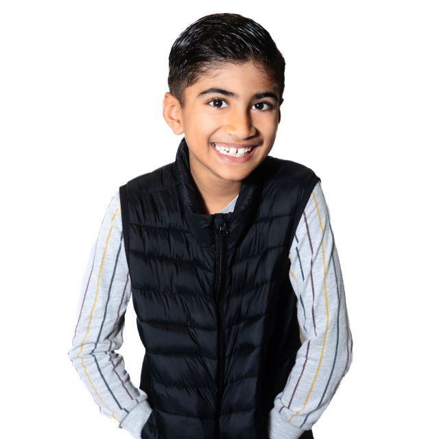 A smiling young boy wearing a black puffy vest over a striped long-sleeve shirt poses against a white background.