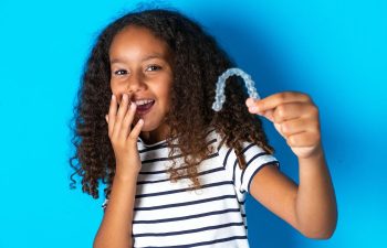 laughing Afro-American young teen girl covering her mouth with one hand and holding an Invisalign aligner in the other one