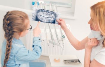 A dentist showing a digital dental imaging to a little girl sitting in a dental chair