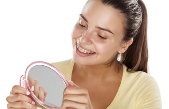 Happy young woman wearing orthodontic braces looking at her teeth in a mirror